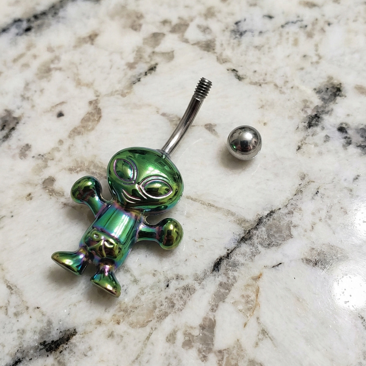 Alien Iridescent Holographic Belly Ring 14G 316L Surgical Steel on a countertop.