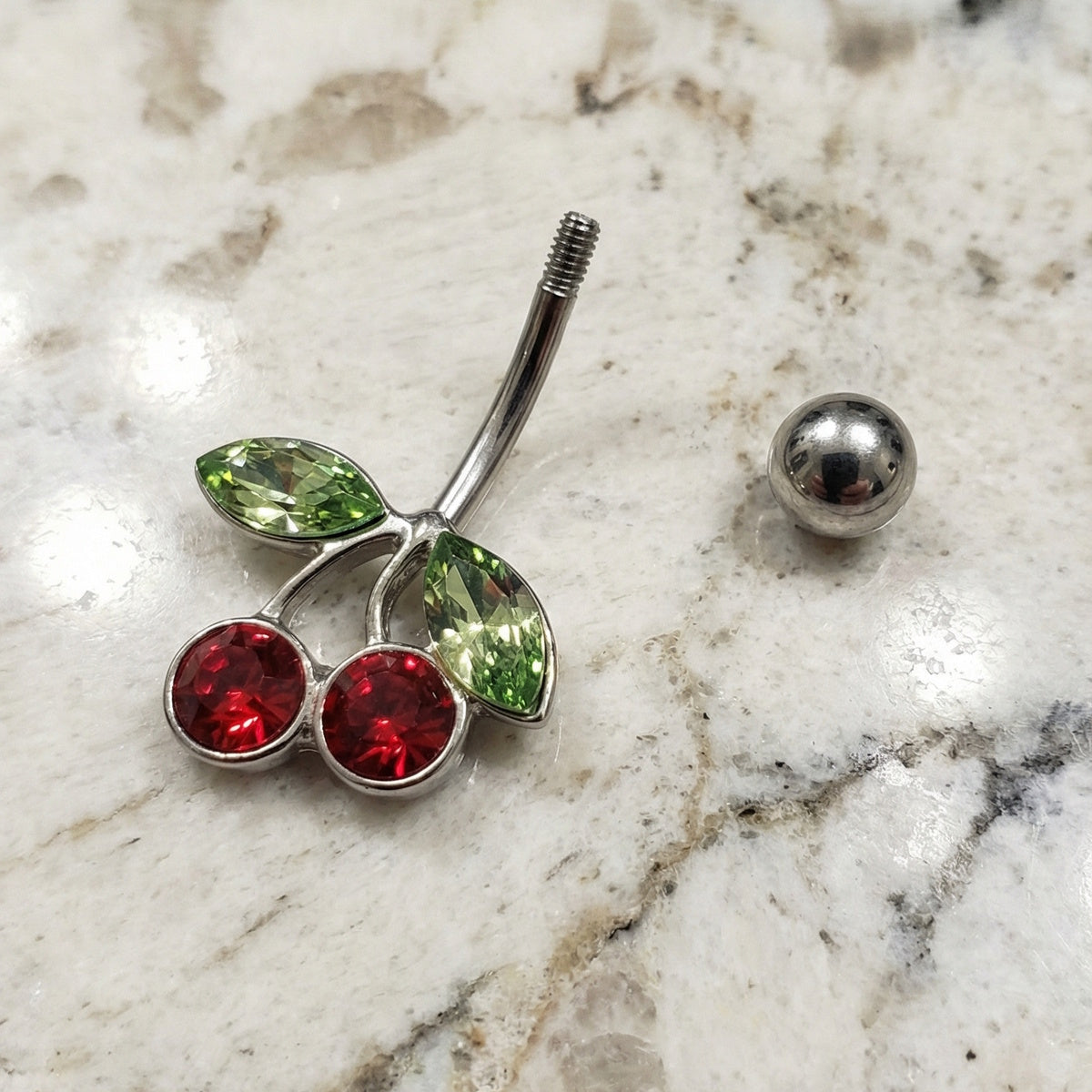Cherry Red Green CZ Belly Ring 14G 316L Surgical Steel on a white granite countertop.