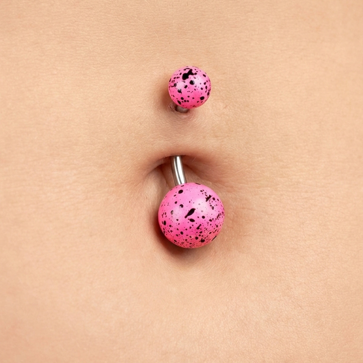Pink splatter belly bar in the belly button piercing of a female.