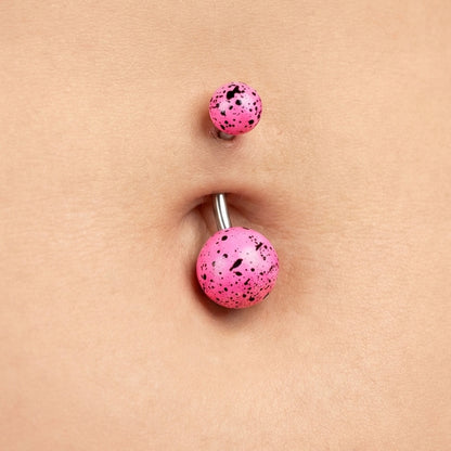 Pink splatter belly bar in the belly button piercing of a female.
